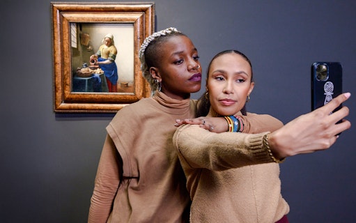 Visitors taking a selfie with Vermeer's "The Milkmaid" painting in the background.