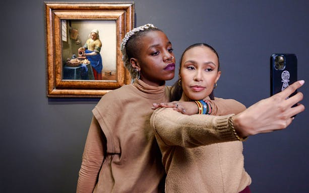 Visitors taking a selfie with Vermeer's "The Milkmaid" painting in the background.