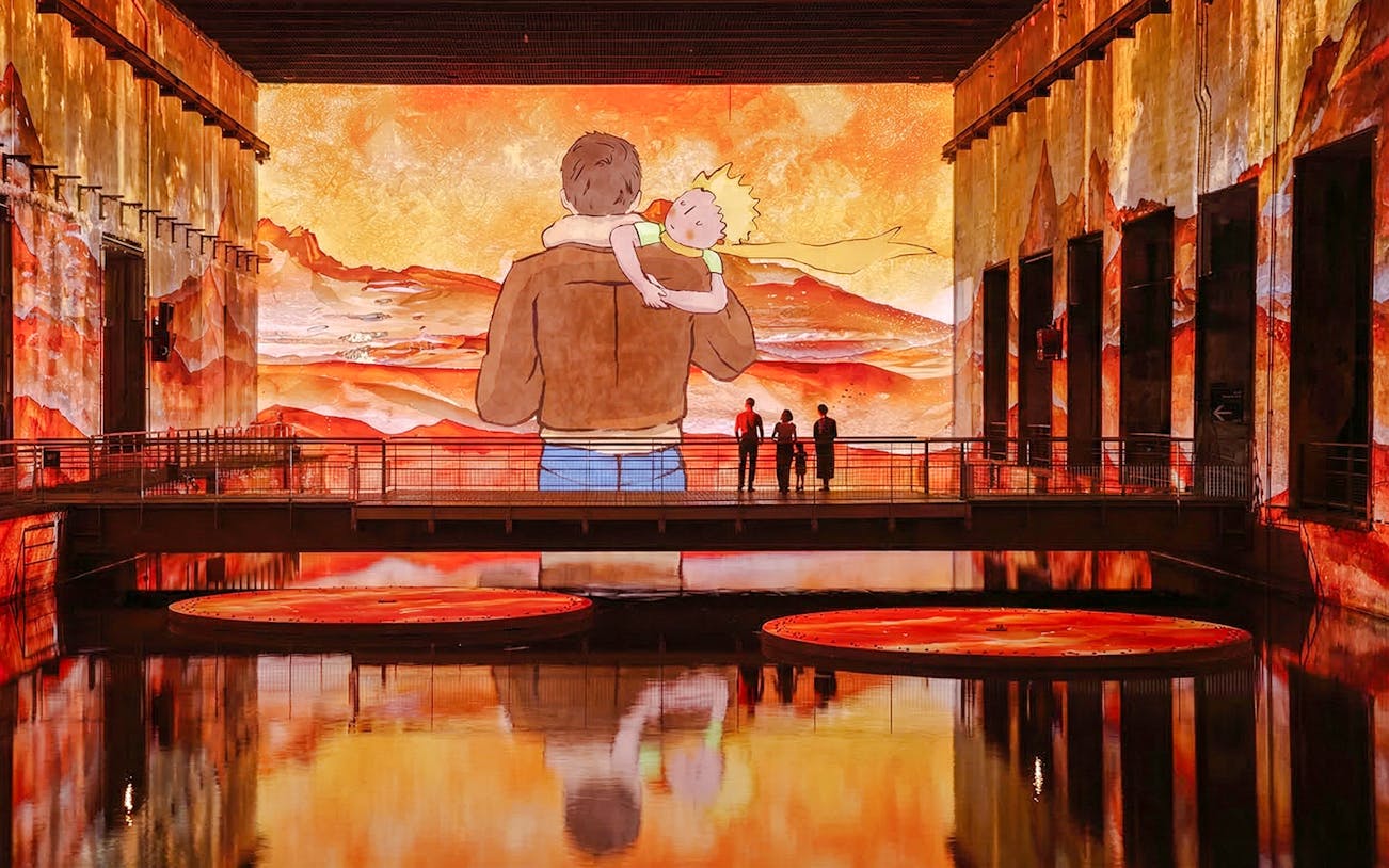 Immersive display of The Little Prince at Bassins des Lumières, Bordeaux, with vibrant orange hues.