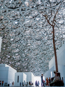 Louvre Abu Dhabi interior with geometric dome and visitors exploring exhibits.