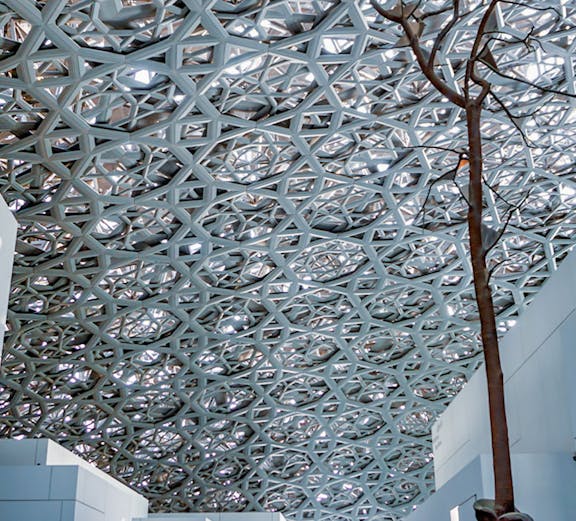 Louvre Abu Dhabi interior with geometric dome and visitors exploring exhibits.
