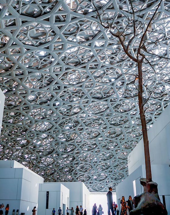 Louvre Abu Dhabi interior with geometric dome and visitors exploring exhibits.
