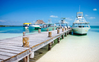 Boats docked at a wooden pier in clear turquoise waters, Cancun.