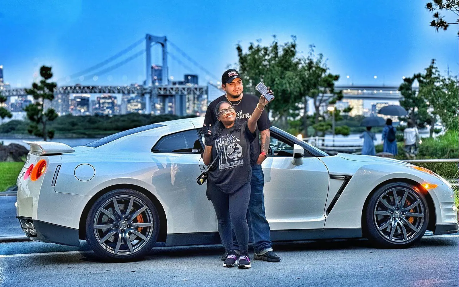 Tokyo skyline with a Nissan GT-R R35 and two people posing for a photo.