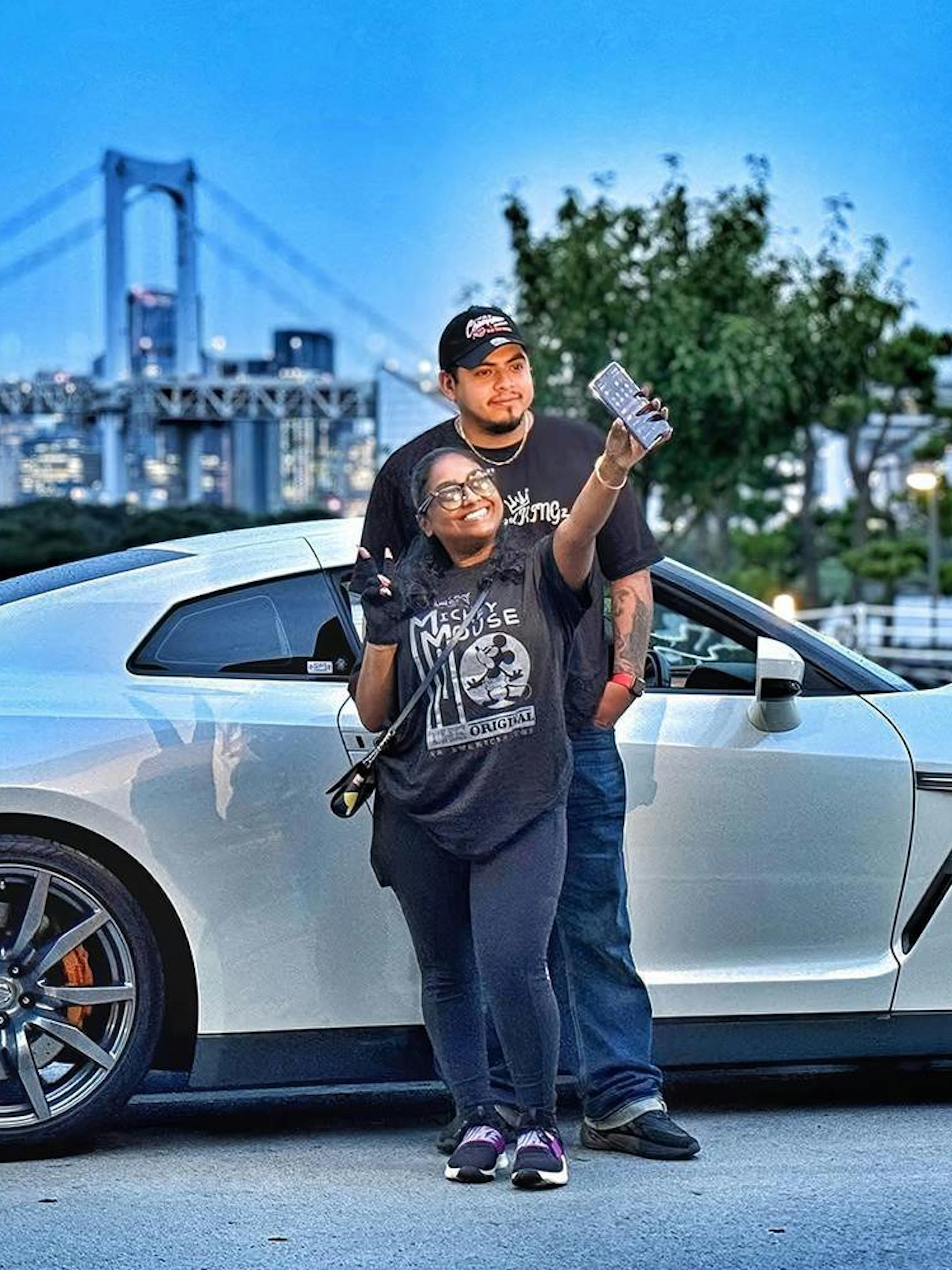 Tokyo skyline with a Nissan GT-R R35 and two people posing for a photo.