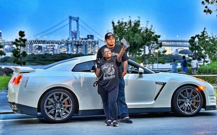 Tokyo skyline with a Nissan GT-R R35 and two people posing for a photo.