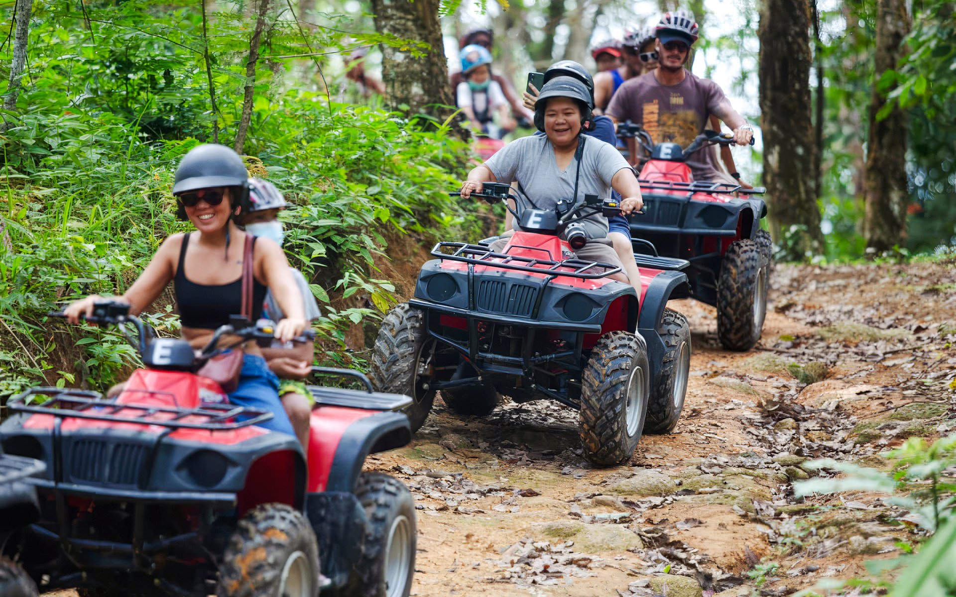 People riding ATVs in a line through a forest trail.