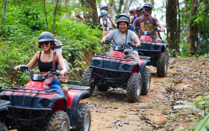 People riding ATVs in a line through a forest trail.