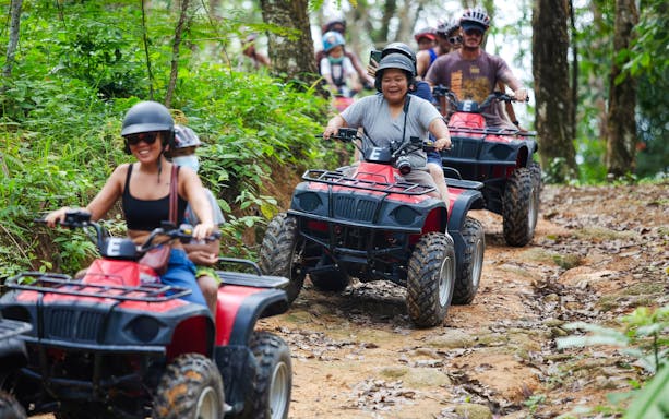 People riding ATVs in a line through a forest trail.