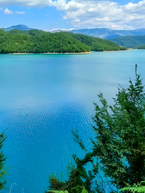 Bovilla Lake surrounded by lush green hills under a blue sky.