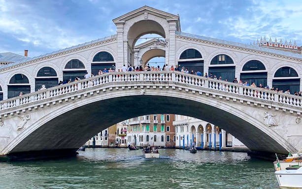 Rialto Bridge over the Grand Canal with boats passing underneath in Venice.