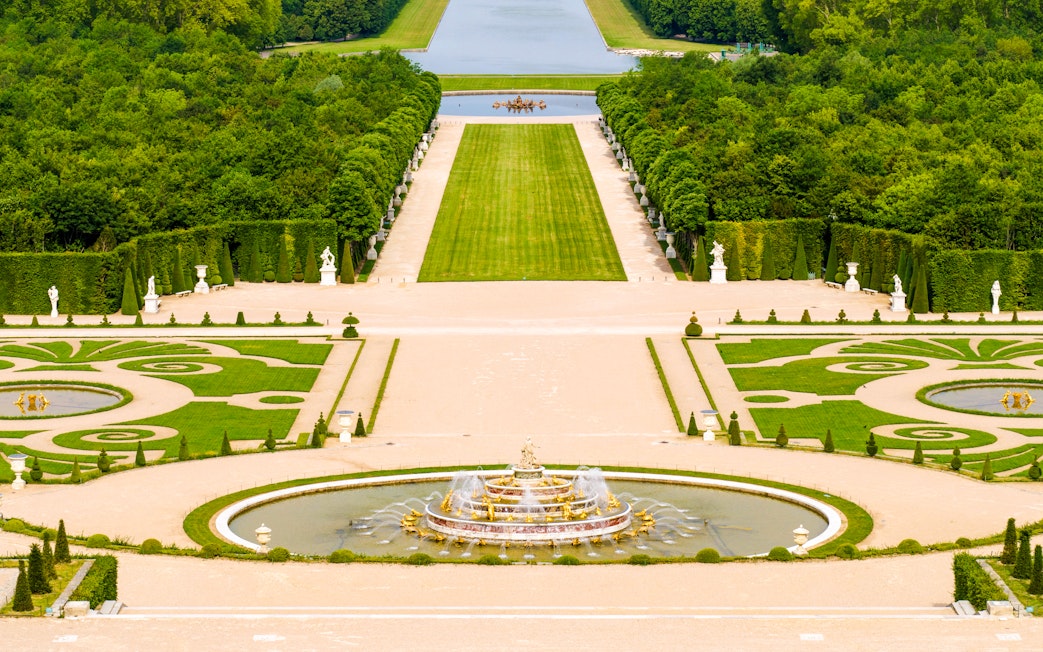 Fountain and gardens at Versailles Palace, Paris, with manicured lawns and statues.