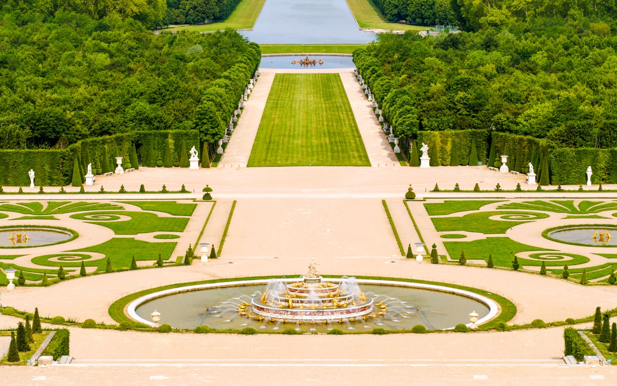 Fountain and gardens at Versailles Palace, Paris, with manicured lawns and statues.