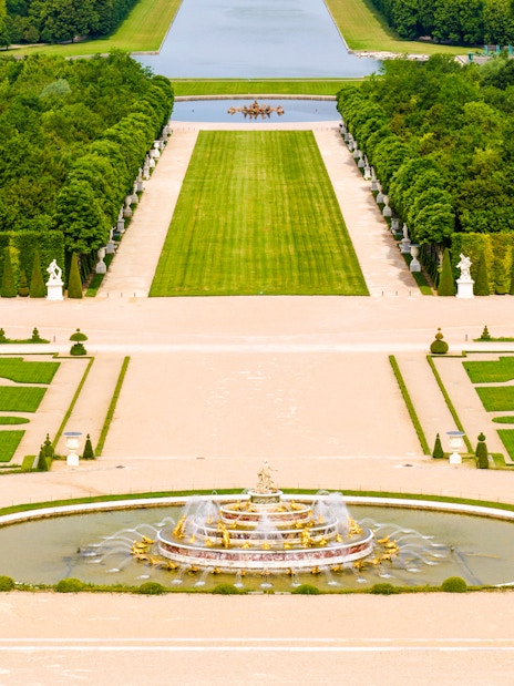 Fountain and gardens at Versailles Palace, Paris, with manicured lawns and statues.