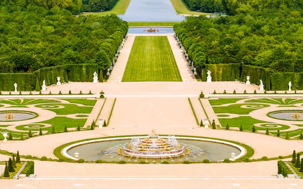 Fountain and gardens at Versailles Palace, Paris, with manicured lawns and statues.