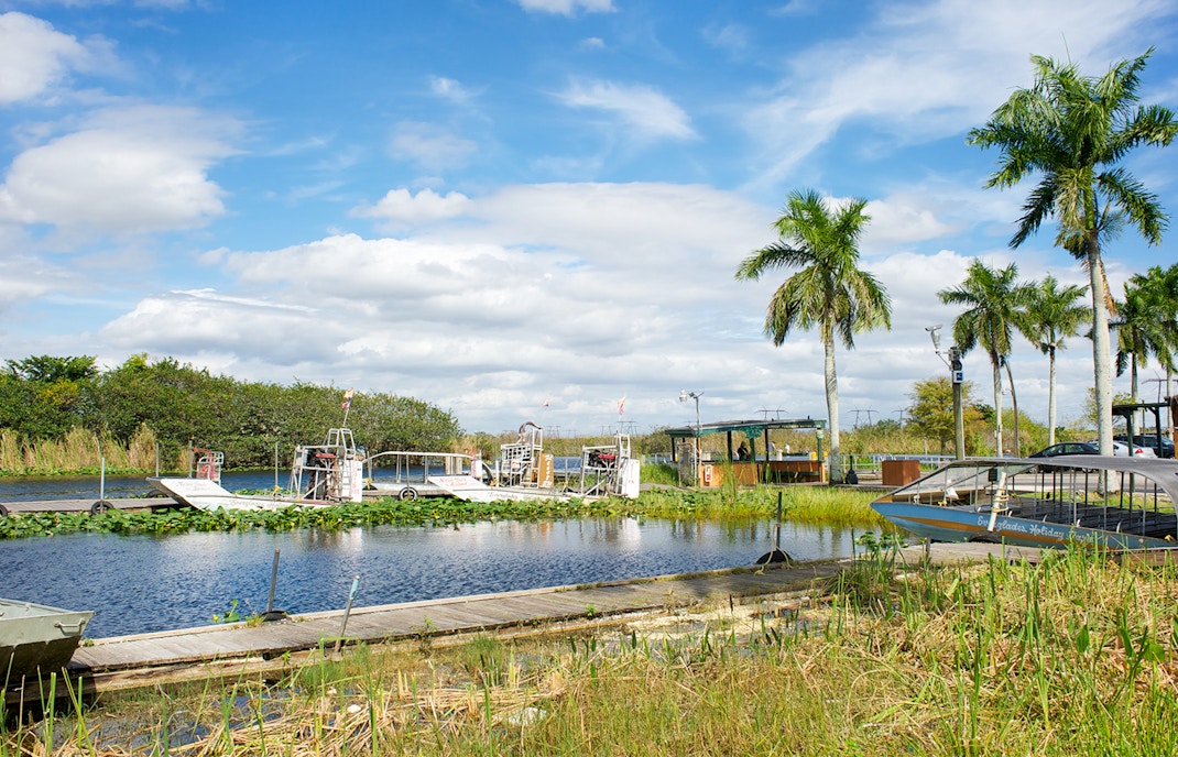 Airboats docked at Coopertown in the Everglades, Florida, surrounded by palm trees and wetlands.
