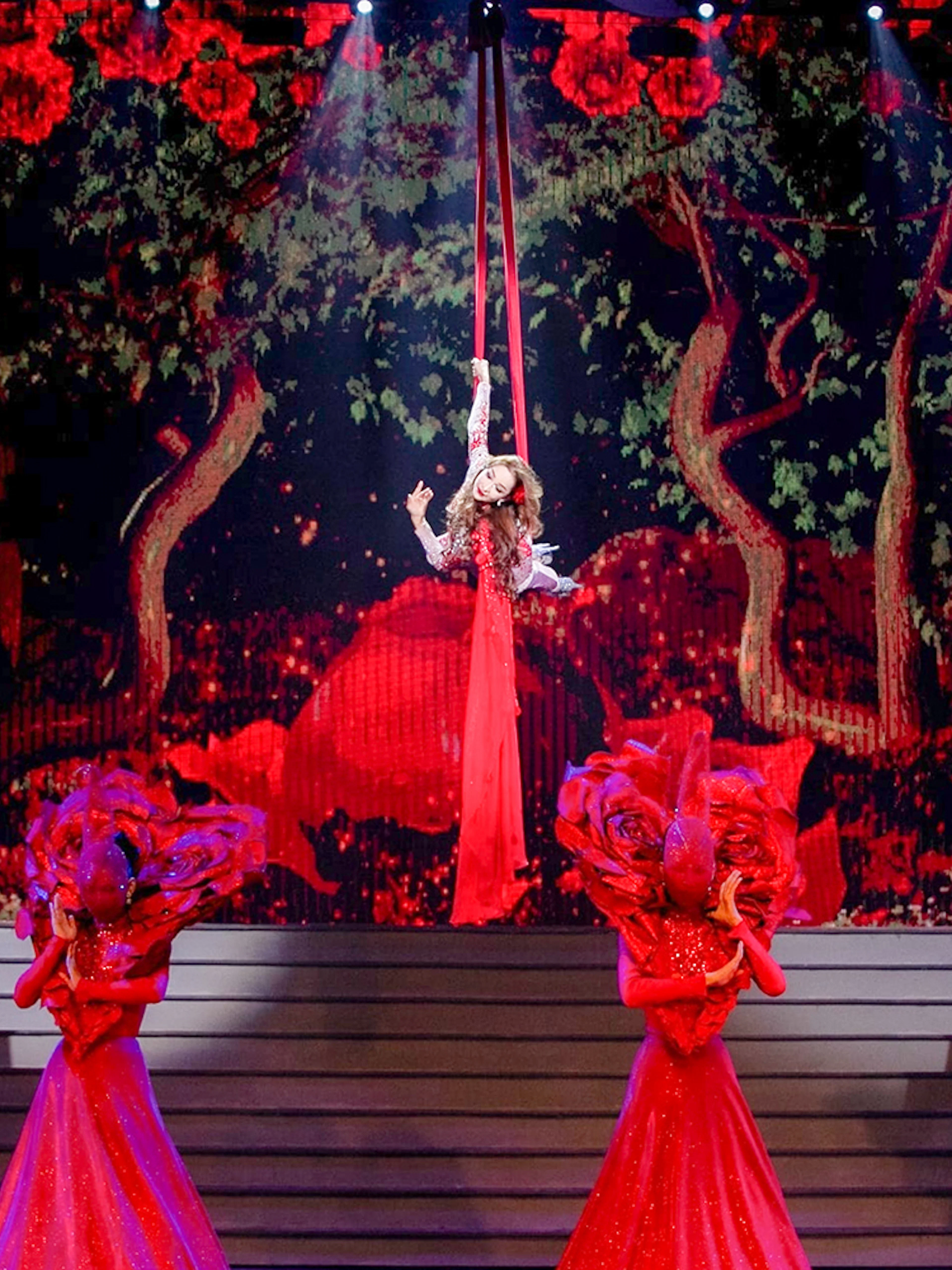 Performer suspended in air with dancers in red costumes at Tiffany's Show.