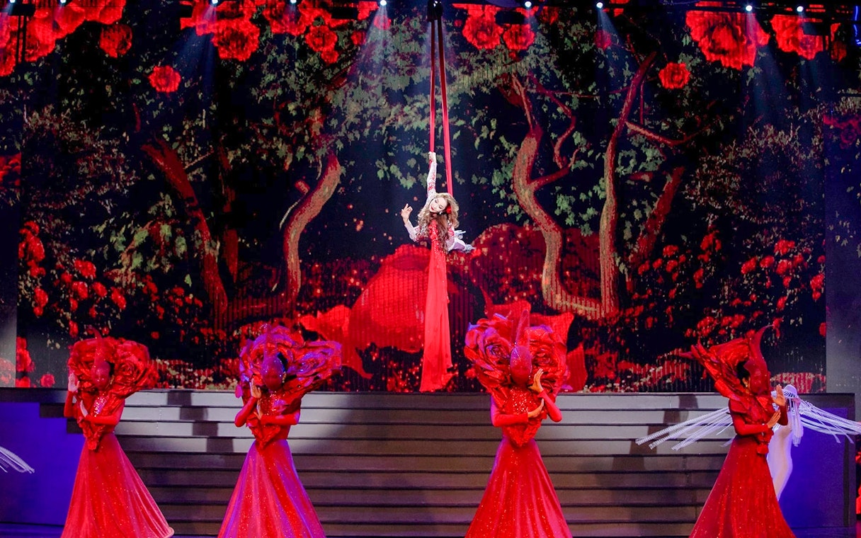 Performer suspended in air with dancers in red costumes at Tiffany's Show.