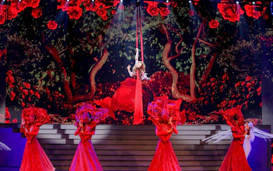 Performer suspended in air with dancers in red costumes at Tiffany's Show.