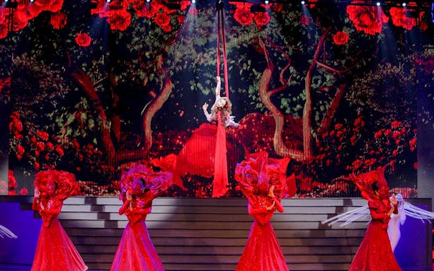 Performer suspended in air with dancers in red costumes at Tiffany's Show.