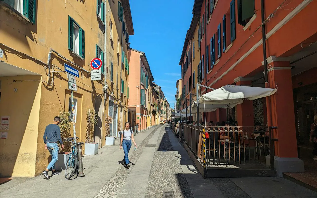 Narrow street in Bologna with colorful buildings and outdoor café seating.