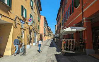 Narrow street in Bologna with colorful buildings and outdoor café seating.