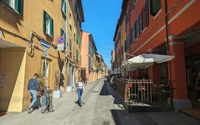 Narrow street in Bologna with colorful buildings and outdoor café seating.