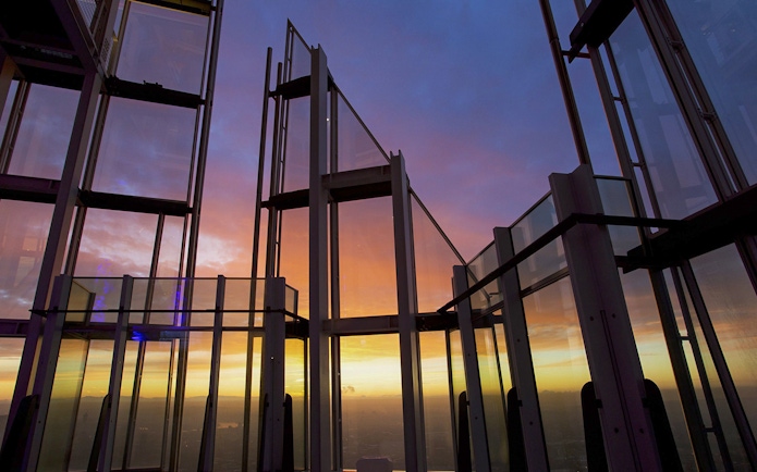 Glass observation deck at sunset with city view.