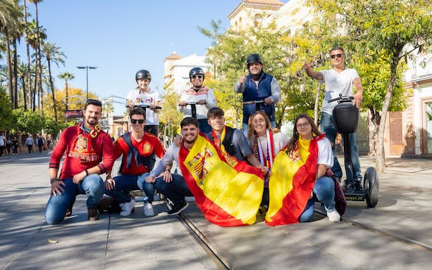 Group enjoying a Segway tour in Seville, Spain, with Spanish flags and sunny street.