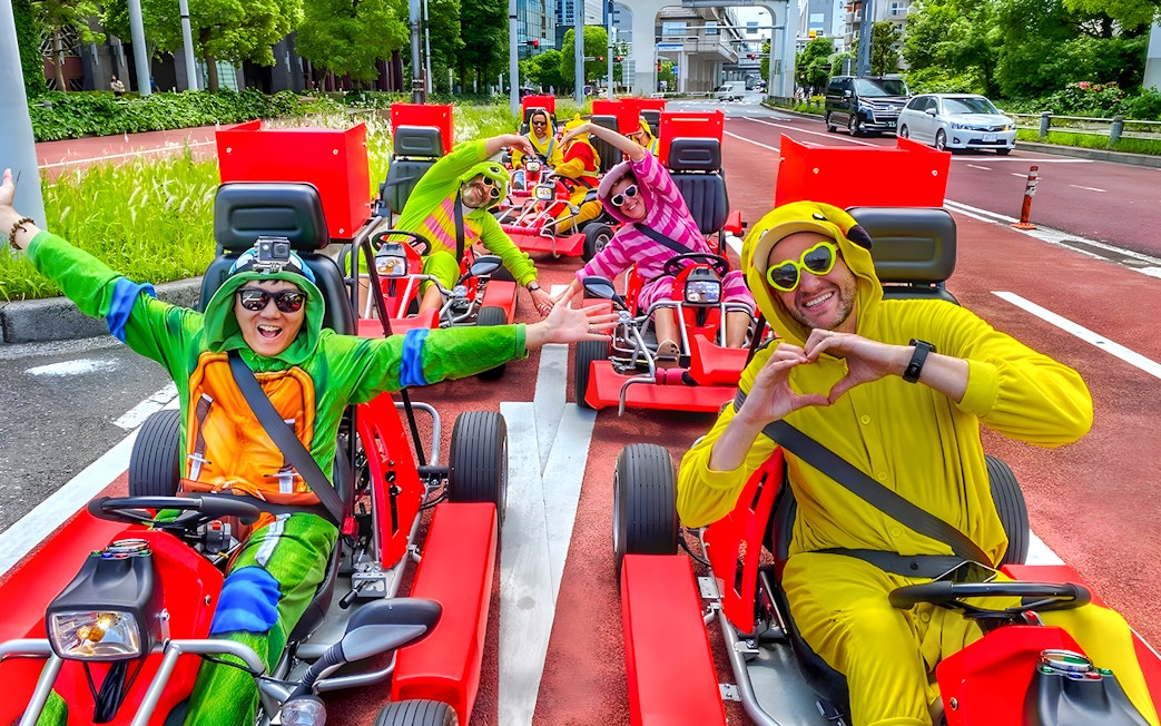 Go-kart riders in costumes driving on a street near Tokyo Bay.