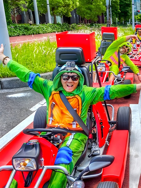 Go-kart riders in costumes driving on a street near Tokyo Bay.