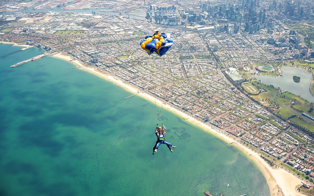 Tandem skydive over St Kilda Beach, Melbourne with cityscape in background.