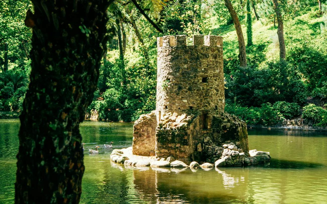 Stone tower in a pond surrounded by lush greenery in Sintra, Portugal.