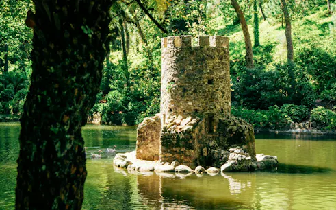 Stone tower in a pond surrounded by lush greenery in Sintra, Portugal.