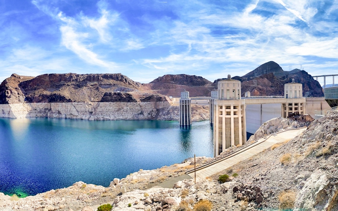 Hoover Dam with pathway leading to Colorado River bank on a sunny morning.