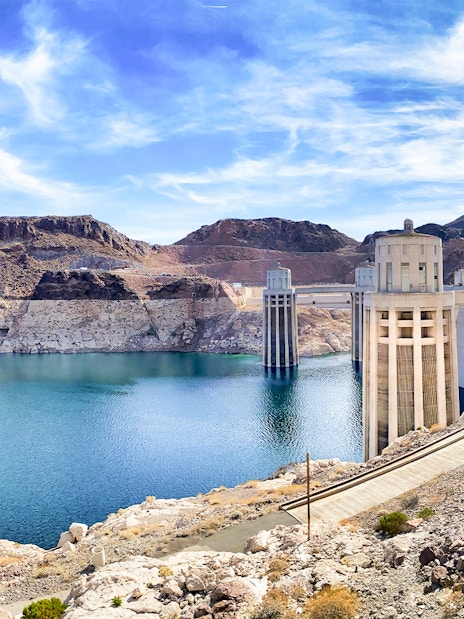 Hoover Dam with pathway leading to Colorado River bank on a sunny morning.