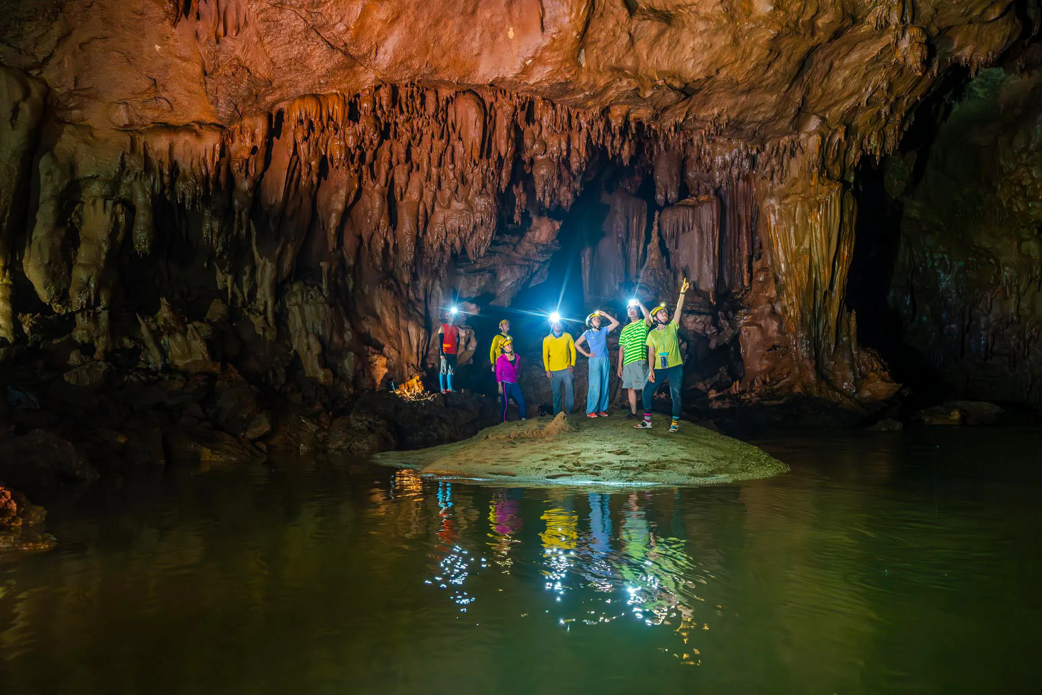 Tourists exploring Phong Nha Cave with headlamps, surrounded by stalactites and water reflections.
