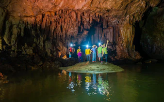 Tourists exploring Phong Nha Cave with headlamps, surrounded by stalactites and water reflections.