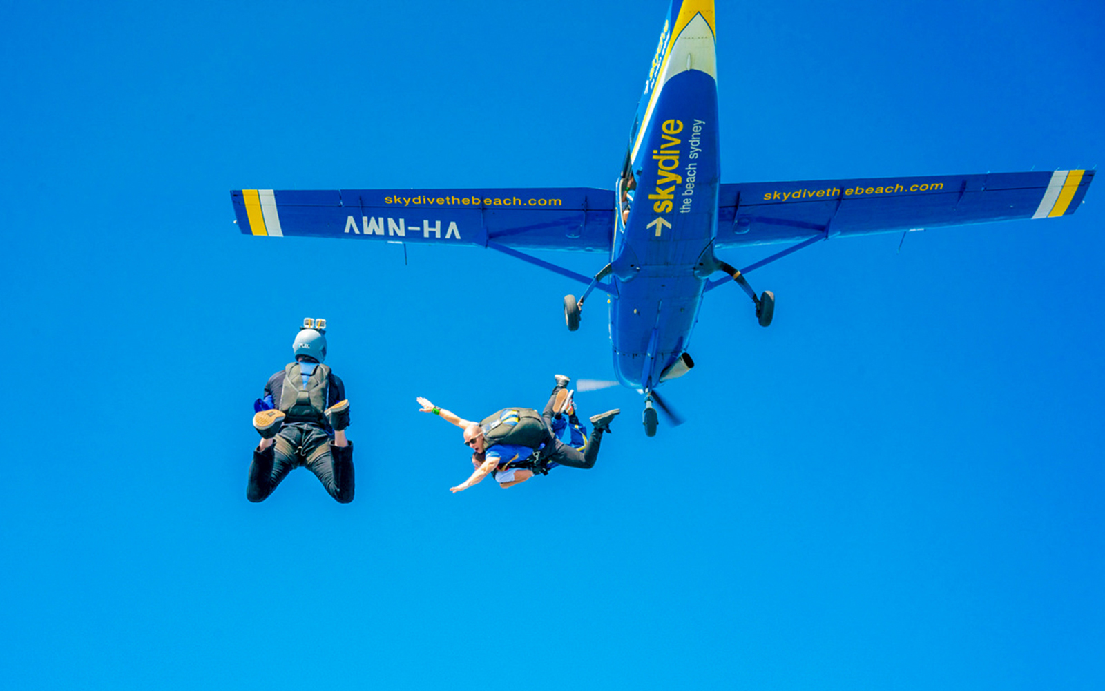 Skydivers jumping from a plane over Byron Bay during a 15,000ft tandem skydive.