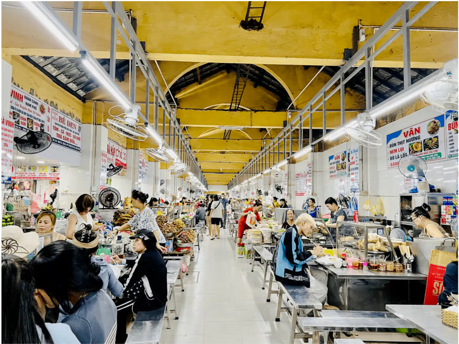 Indoor market scene in Da Nang with people dining and shopping at food stalls.
