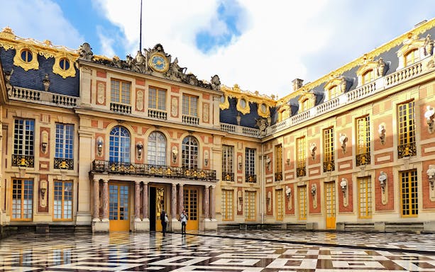 Palace of Versailles courtyard with ornate architecture and French flag.