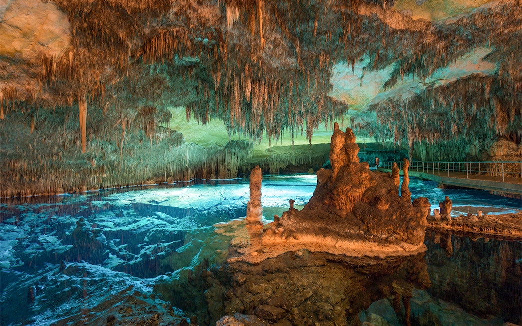 Stalactites and stalagmites in the illuminated Caves of Drach, Mallorca, with a reflective underground lake.