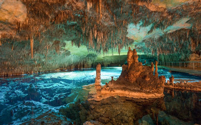 Stalactites and stalagmites in the illuminated Caves of Drach, Mallorca, with a reflective underground lake.