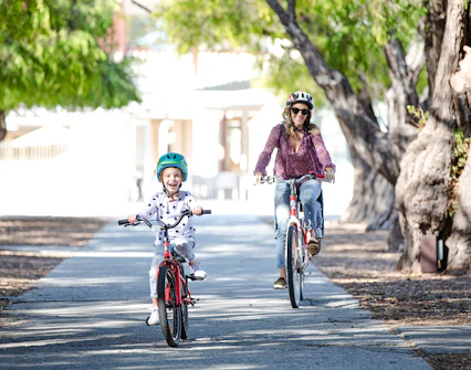 Woman and child cycling on a tree-lined path on Rottnest Island, Western Australia.