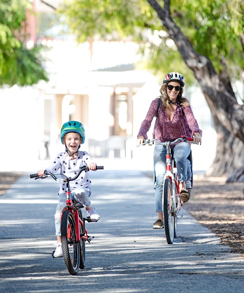 Woman and child cycling on a tree-lined path on Rottnest Island, Western Australia.