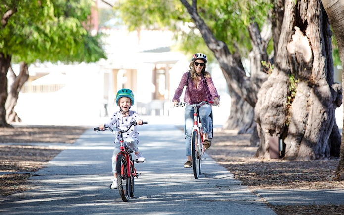 Woman and child cycling on a tree-lined path on Rottnest Island, Western Australia.