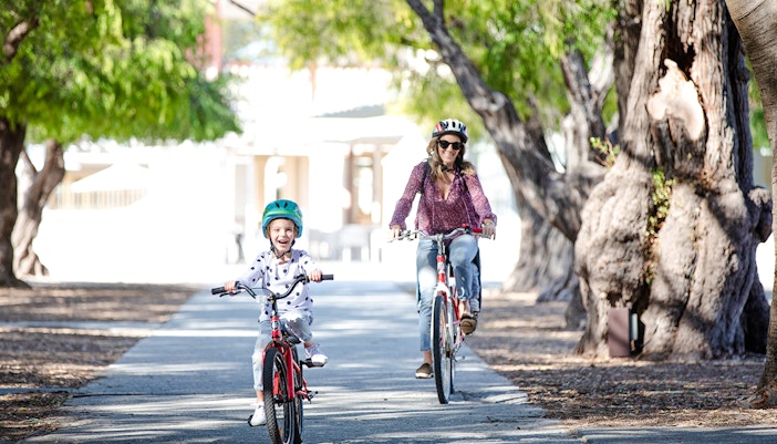 Woman and child cycling on a tree-lined path on Rottnest Island, Western Australia.