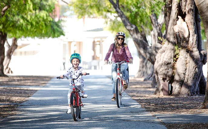 Woman and child cycling on a tree-lined path on Rottnest Island, Western Australia.