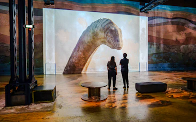 Visitors viewing dinosaur projection at Prehistoric Planet exhibition, Atelier des Lumières.