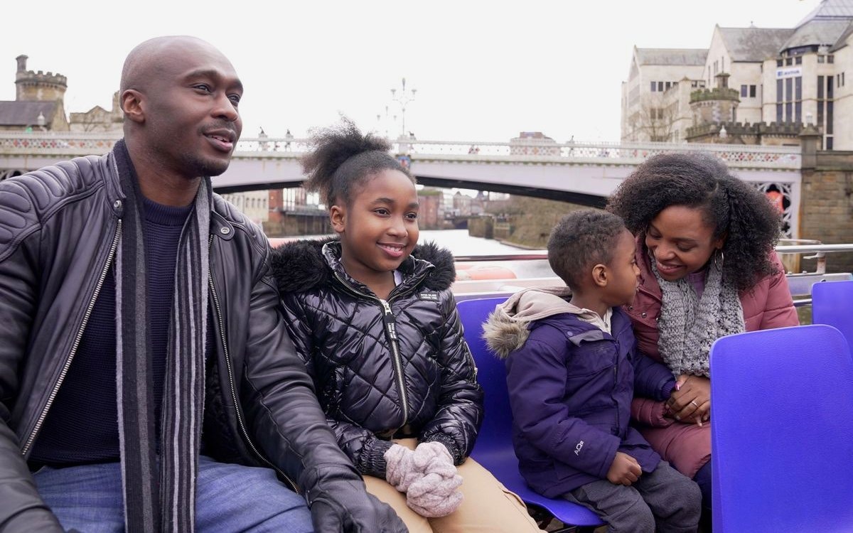 Family enjoying York sightseeing cruise with historic bridge in background.